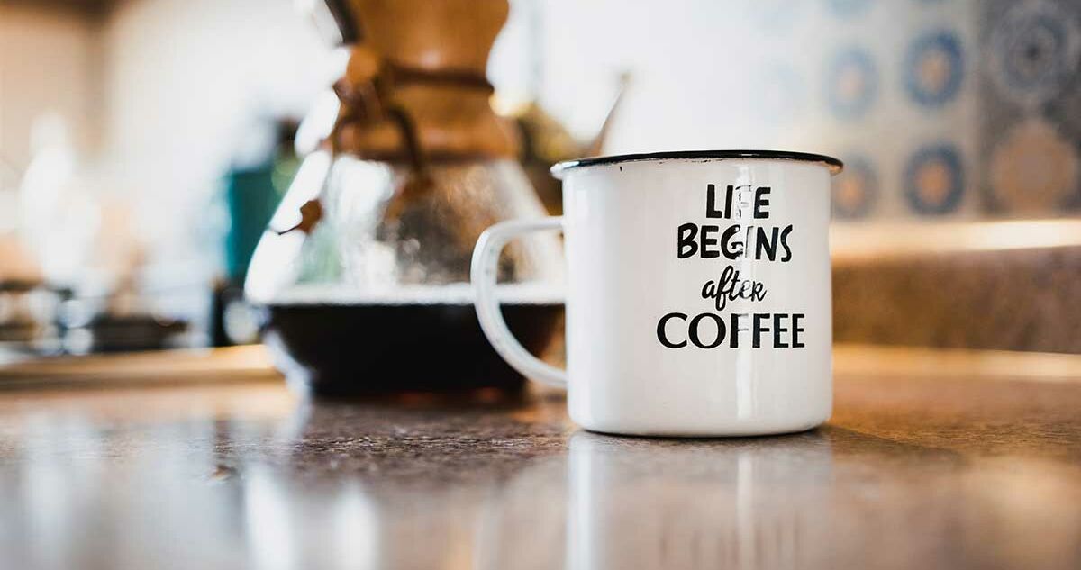 Beschriftete Emaille-Tasse neben einer Kanne mit frisch gebrühtem Kaffee